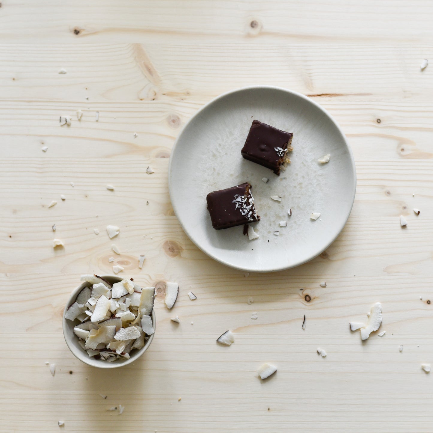 Aufgeschnittener Nounty Kokosriegel mit Kokosfüllung, daneben Datteln und Kokosraspeln