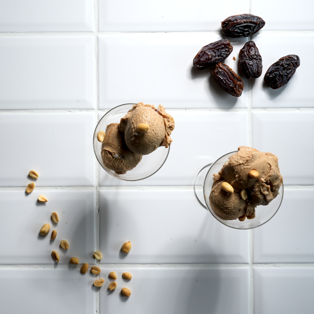 Veganes Dattel-Eis mit Karamell-Swirl in einer Schale, bestreut mit gerösteten Erdnüssen und Fleur de Sel, im Hintergrund frische Medjool-Datteln von diiszwii