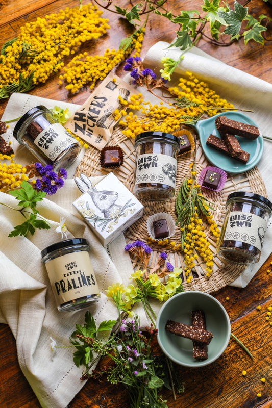 Liebevoll dekorierter Ostertisch mit diiszwii Produkten: ZH-Nickers und Pralinen in festlicher Osterverpackung, arrangiert neben einem eleganten Tuch und frischen Blumen, die eine fröhliche und herzliche Atmosphäre schaffen.