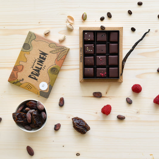 12er Pralinenbox von oben – offene Verpackung mit handgemachten Dattel-Pralinen, Rohstoffe und Schokolade mit Kokosblütenzucker sichtbar