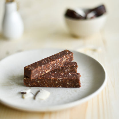 Natürliche Zutaten für den Barohni Kokos Riegel – Cashews, Kokosraspeln und Datteln, unscharf im Hintergrund