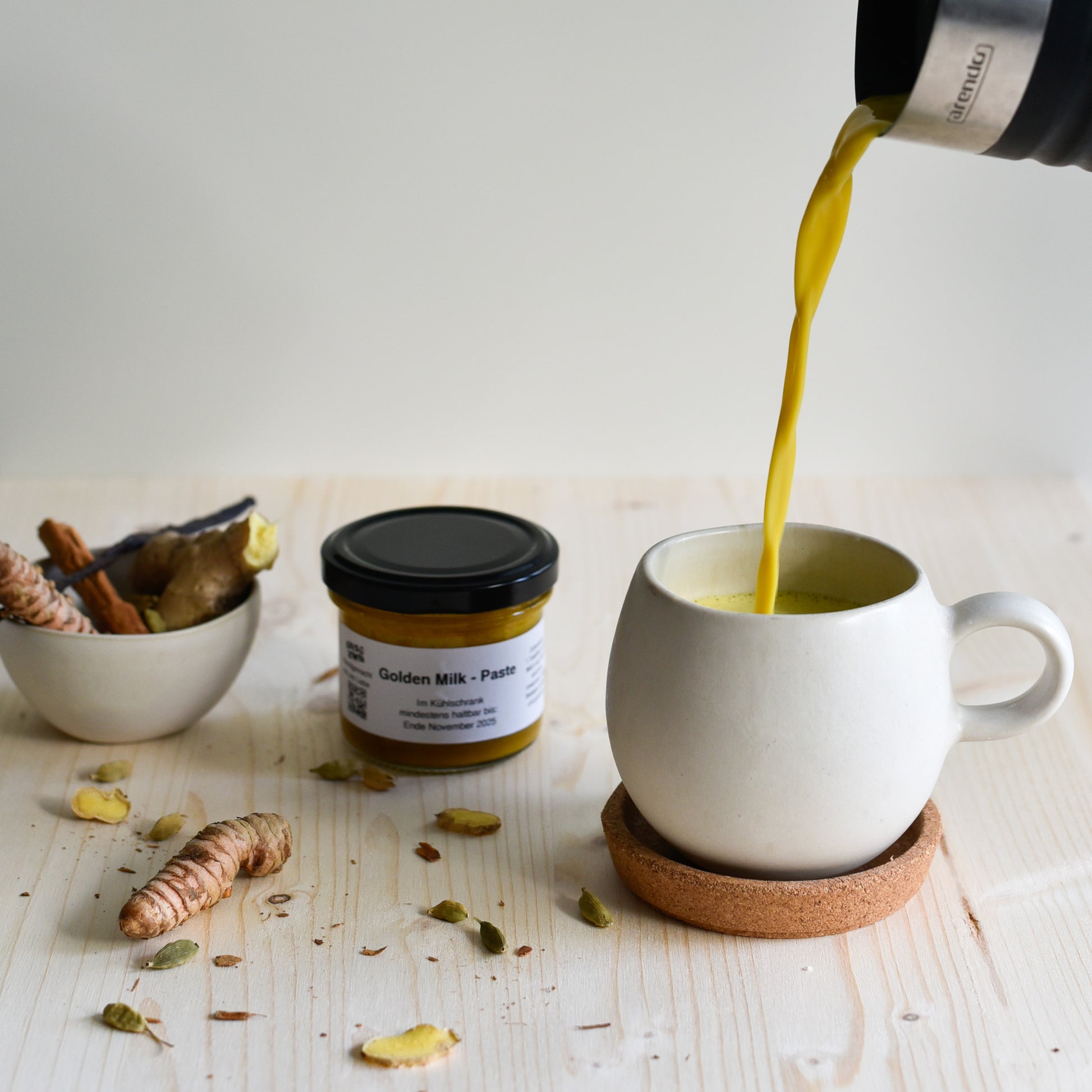 Golden Milk mit Kurkuma-Paste – gelbe Latte wird in Tasse gegossen, Zutaten im Hintergrund sichtbar