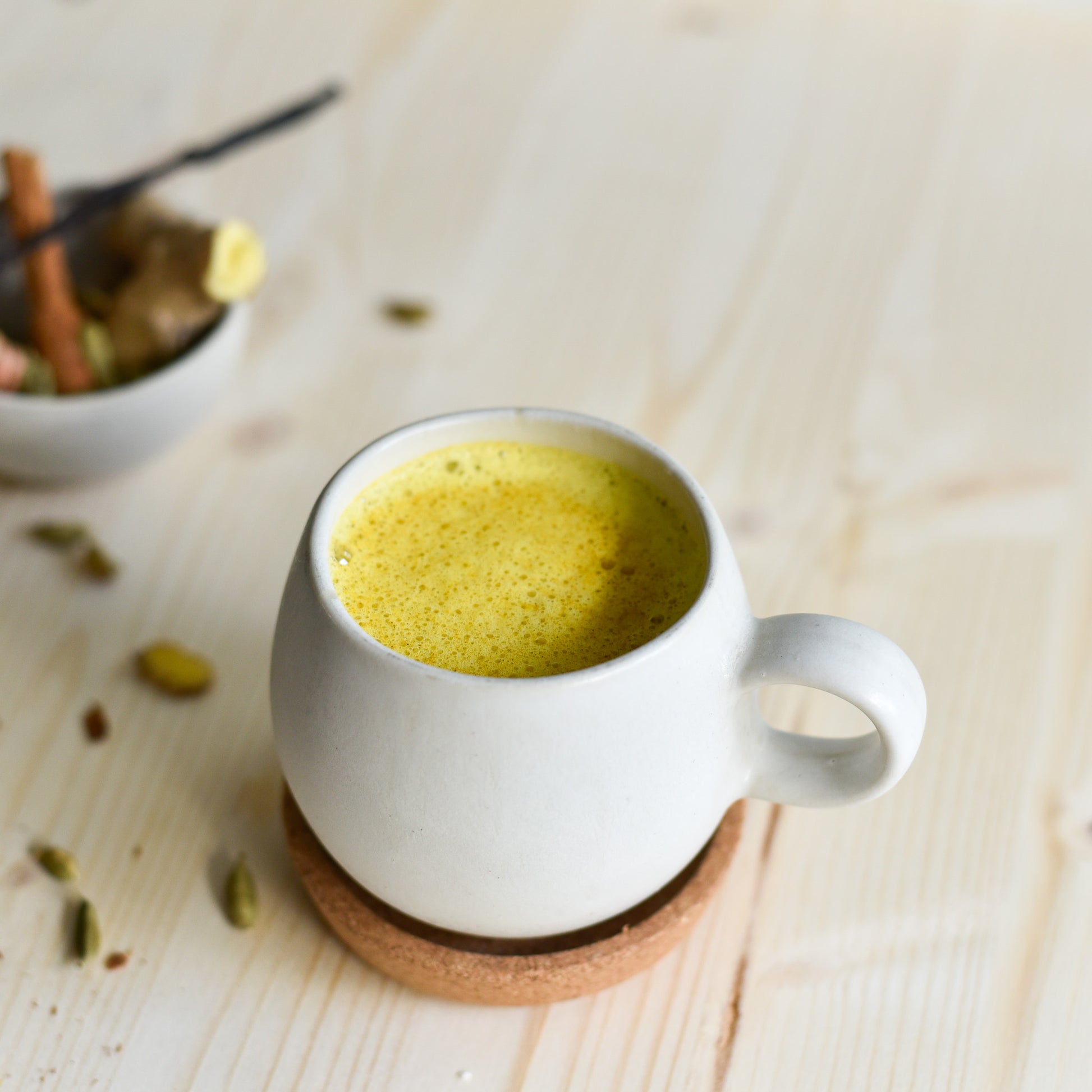 Tasse Golden Milk zubereitet mit handgemachter Kurkuma-Paste, daneben frische Zutaten