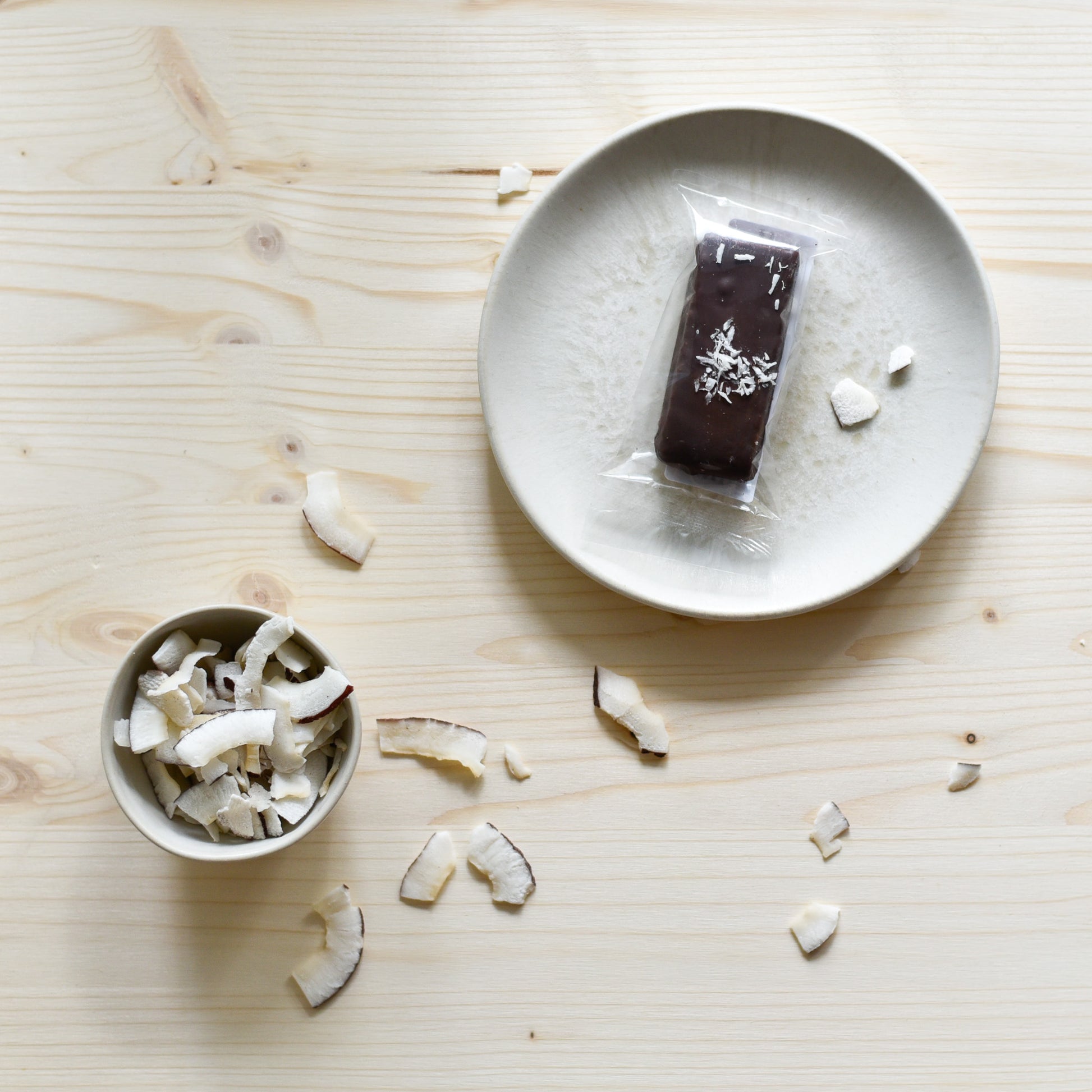 Nounty Kokosriegel verpackt auf Teller mit Datteln und Kokosraspeln daneben – handgemacht in Schlieren