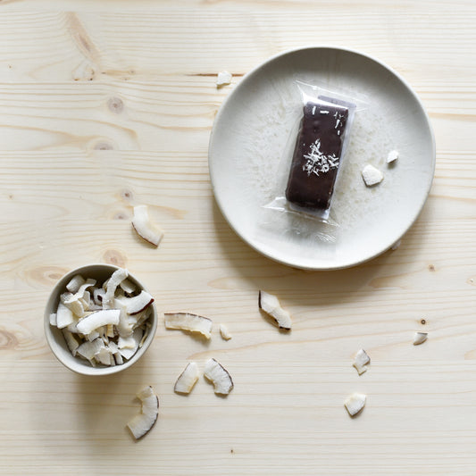 Nounty Kokosriegel verpackt auf Teller mit Datteln und Kokosraspeln daneben – handgemacht in Schlieren